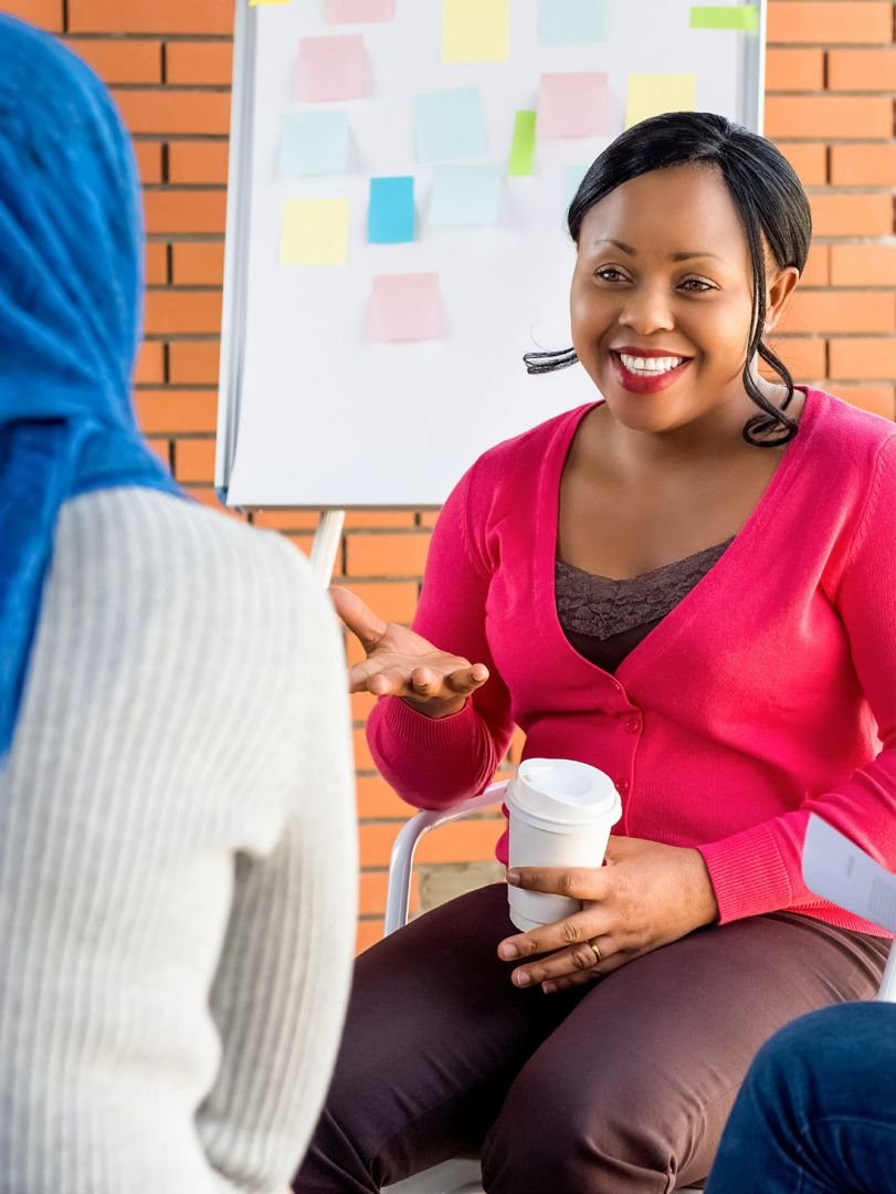A person smiling and talking with a coffee cup in their hand